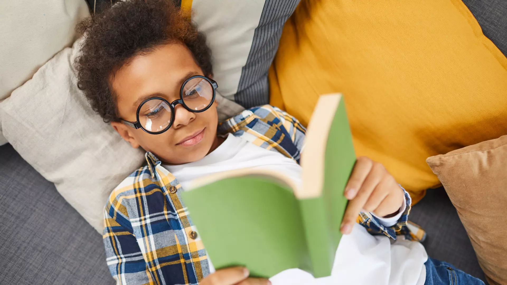 Pojke med glasögon och rutig skjorta  läser en grön bok