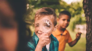 Barn i naturen där en av pojkarna tittar glatt igenom ett förstoringsglas