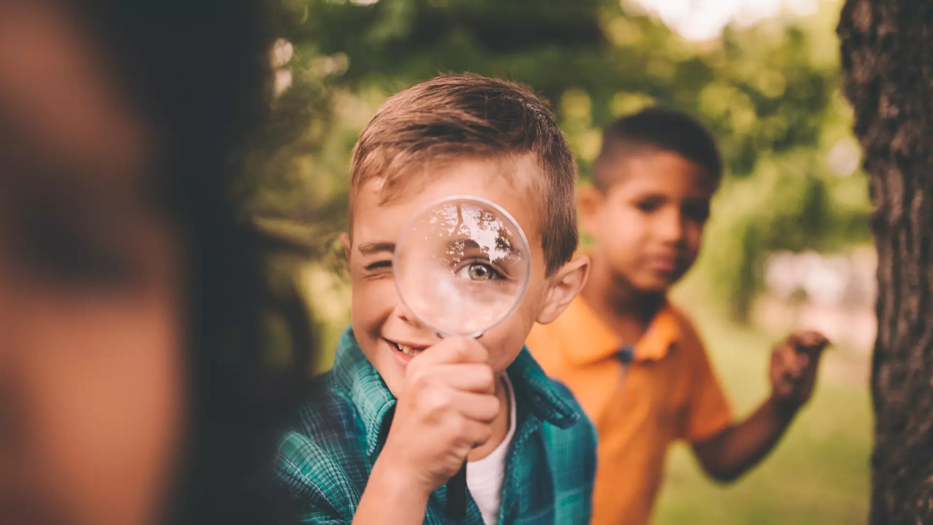 Barn i naturen där en av pojkarna tittar glatt igenom ett förstoringsglas